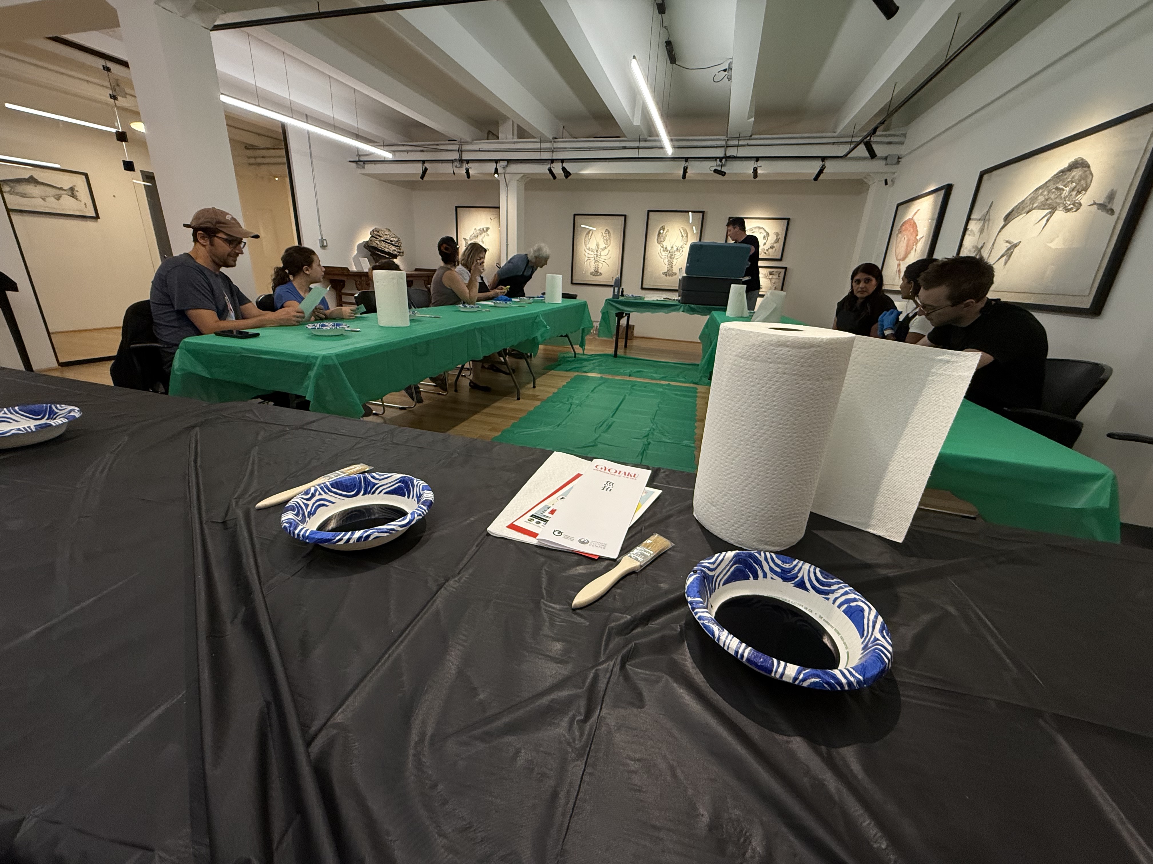 Gyotaku classroom before printing started.
 3 tables all covered with plastic sheeting. One bowl of ink and some ink brushes, and a large roll of paper towels.